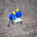Top view two engineers discussing over blueprint on land at wind turbine site.
